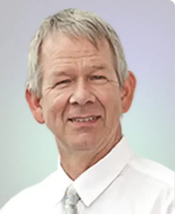 Portr&auml;tfoto von Gerhard Winkler mit kurzen grauen Haaren, einem freundlichen L&auml;cheln, in einem wei&szlig;en Hemd und einer Krawatte vor hellem Hintergrund.