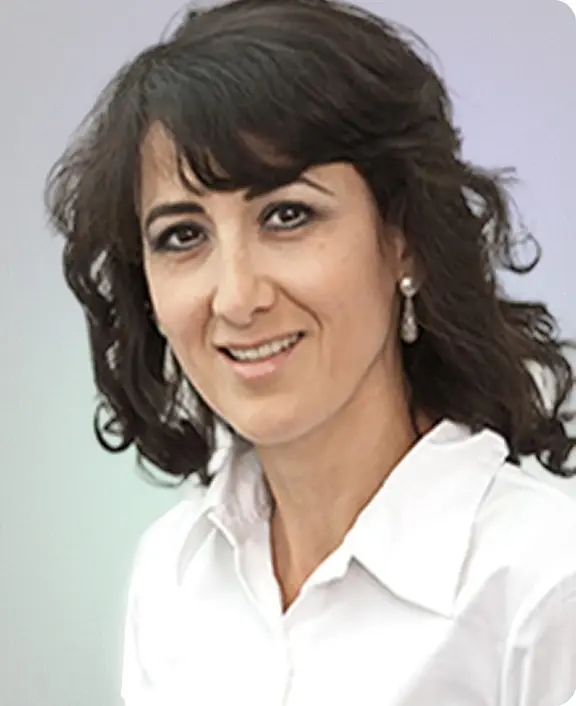 Portr&auml;tfoto von Prof. Dr. med. Alaleh Raji mit dunklen, lockigen Haaren, wei&szlig;er Bluse und freundlichem Ausdruck vor hellem Hintergrund.