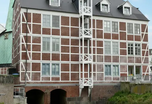 Backsteingeb&auml;ude mit wei&szlig;em Fachwerk &uuml;ber einem Kanal, mit mehreren Fenstern und einem kleinen Balkon an der Vorderseite.